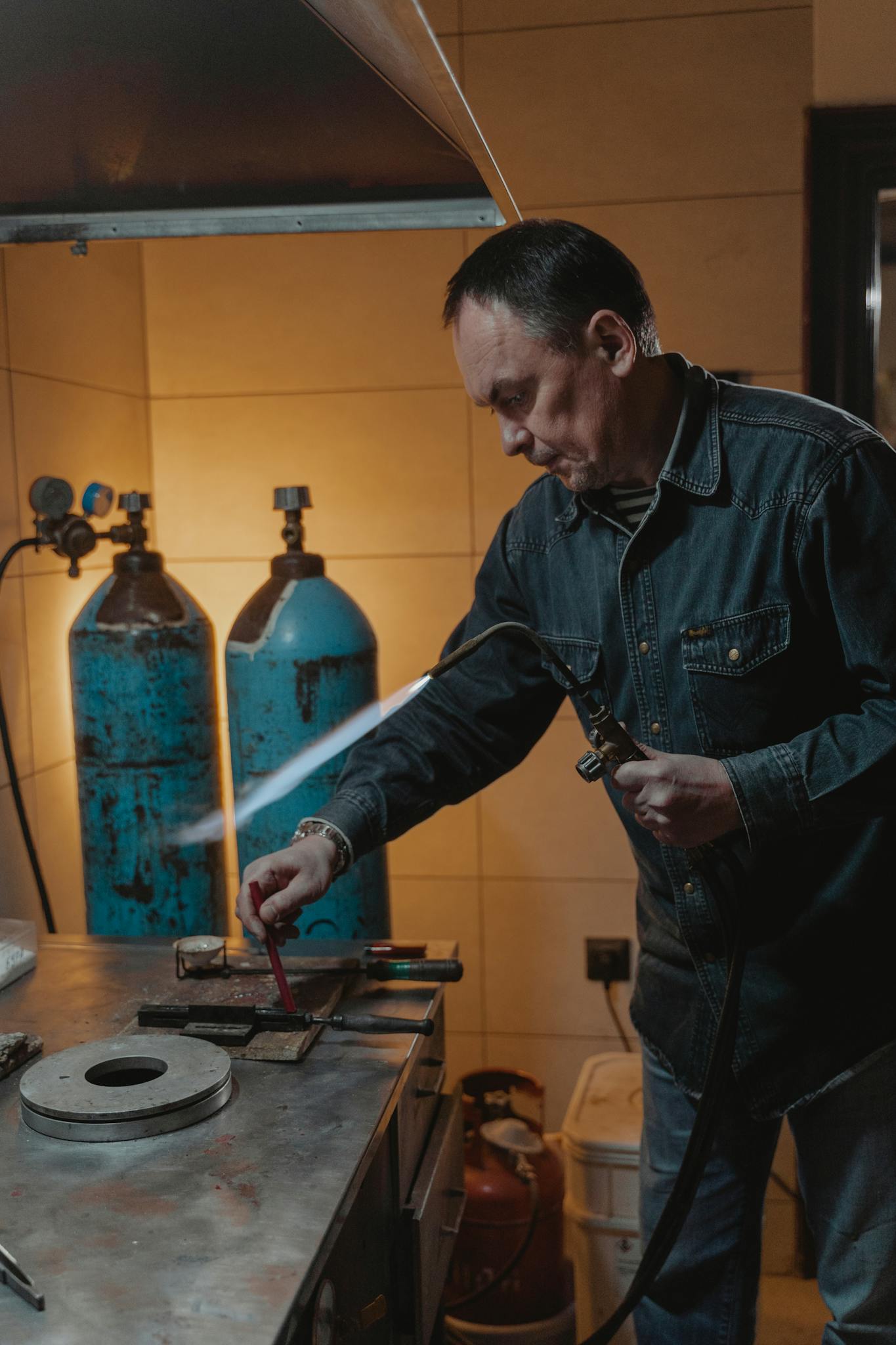A man using a welding torch in a metal workshop with gas cylinders in the background.